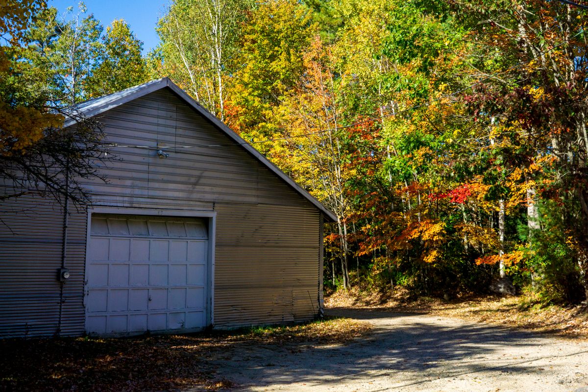 Metal garage with roll-up door among autumn trees